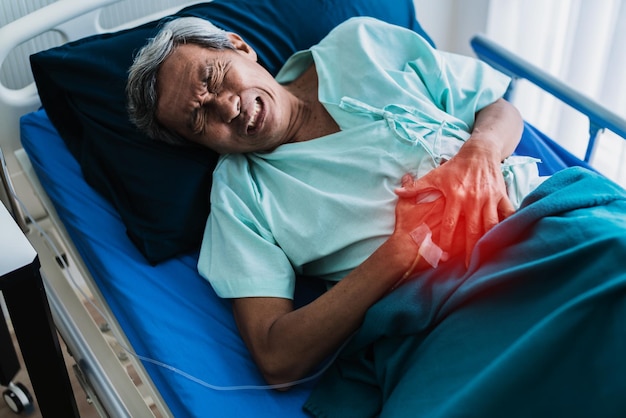 Elderly patient lying in a hospital bed holding his abdomen in pain